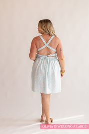Woman wearing a light blue dress with criss-cross straps on a plain background