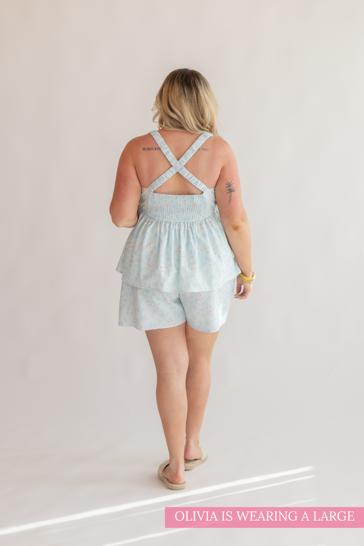 Woman wearing a light blue romper with criss-cross straps on a plain background