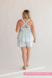 Woman wearing a light blue romper with criss-cross straps on a plain background
