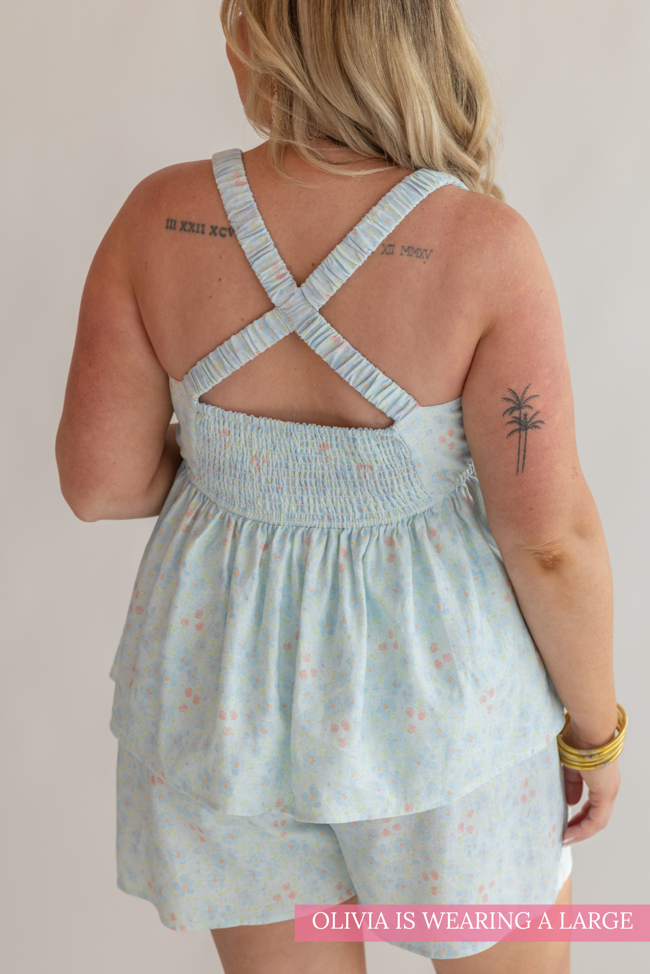 Woman wearing a light blue dress with floral pattern, standing against a plain background.