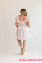 Woman wearing a light pink dress with floral patterns on a white background