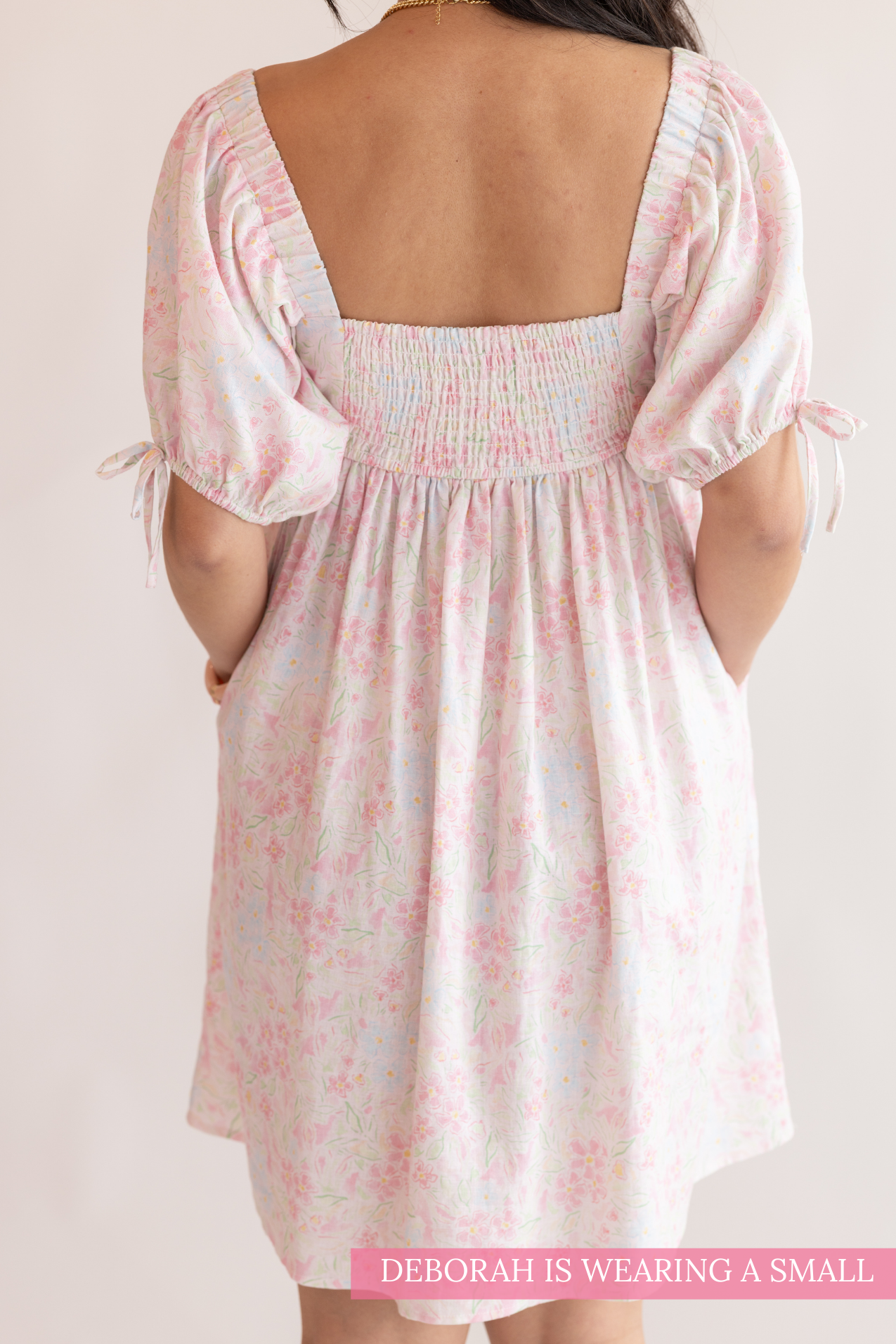 White dress with pink floral pattern worn by a person on a plain background