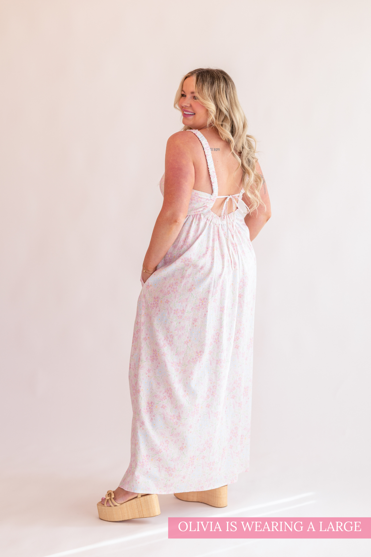 Woman wearing a white dress with pink floral pattern on a plain background