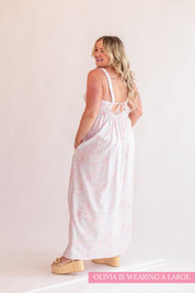 Woman wearing a white dress with pink floral pattern on a plain background