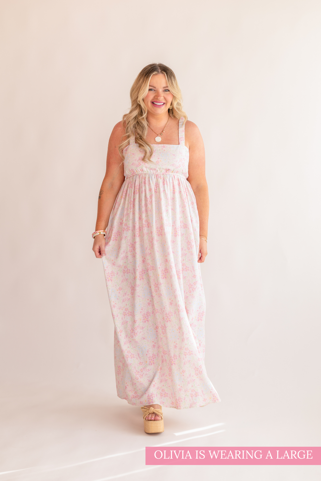 Woman wearing a white sleeveless top and pink floral dress on a beige background