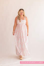 Woman wearing a white sleeveless top and pink floral dress on a beige background