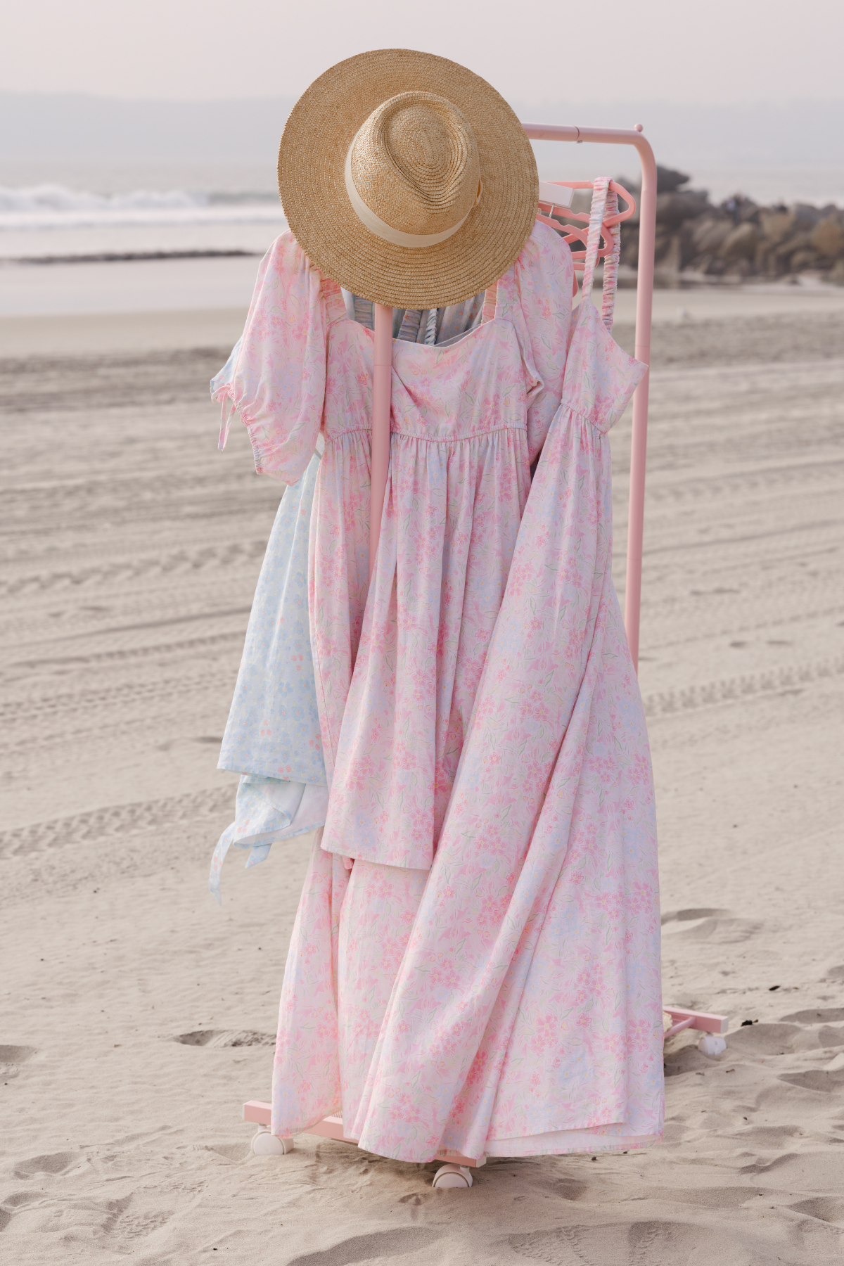 Pink clothing rack with floral spring dresses and a sunhat on a beach