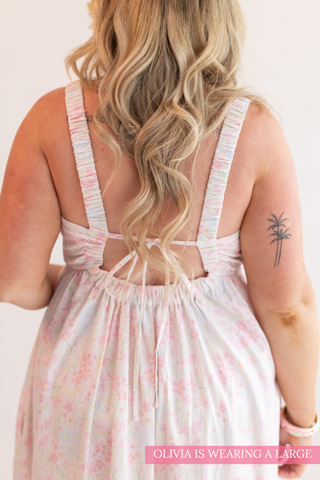 Woman wearing a light pink floral dress with thin straps on a plain background