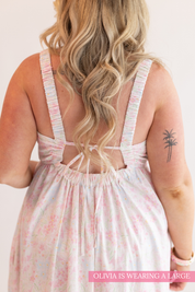 Woman wearing a light pink floral dress with thin straps on a plain background