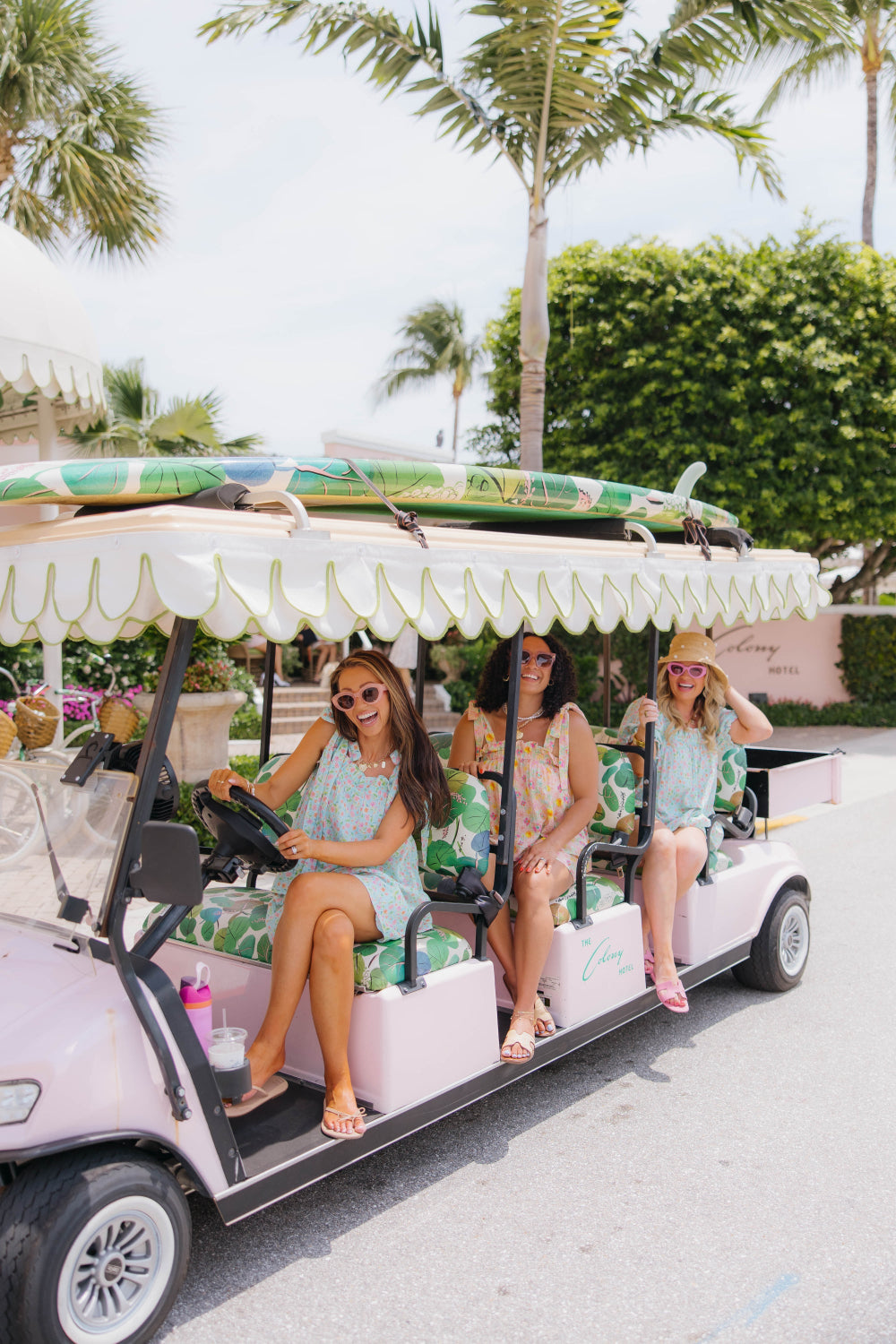 Group of women in a decorated golf cart with palm trees and greenery in the background