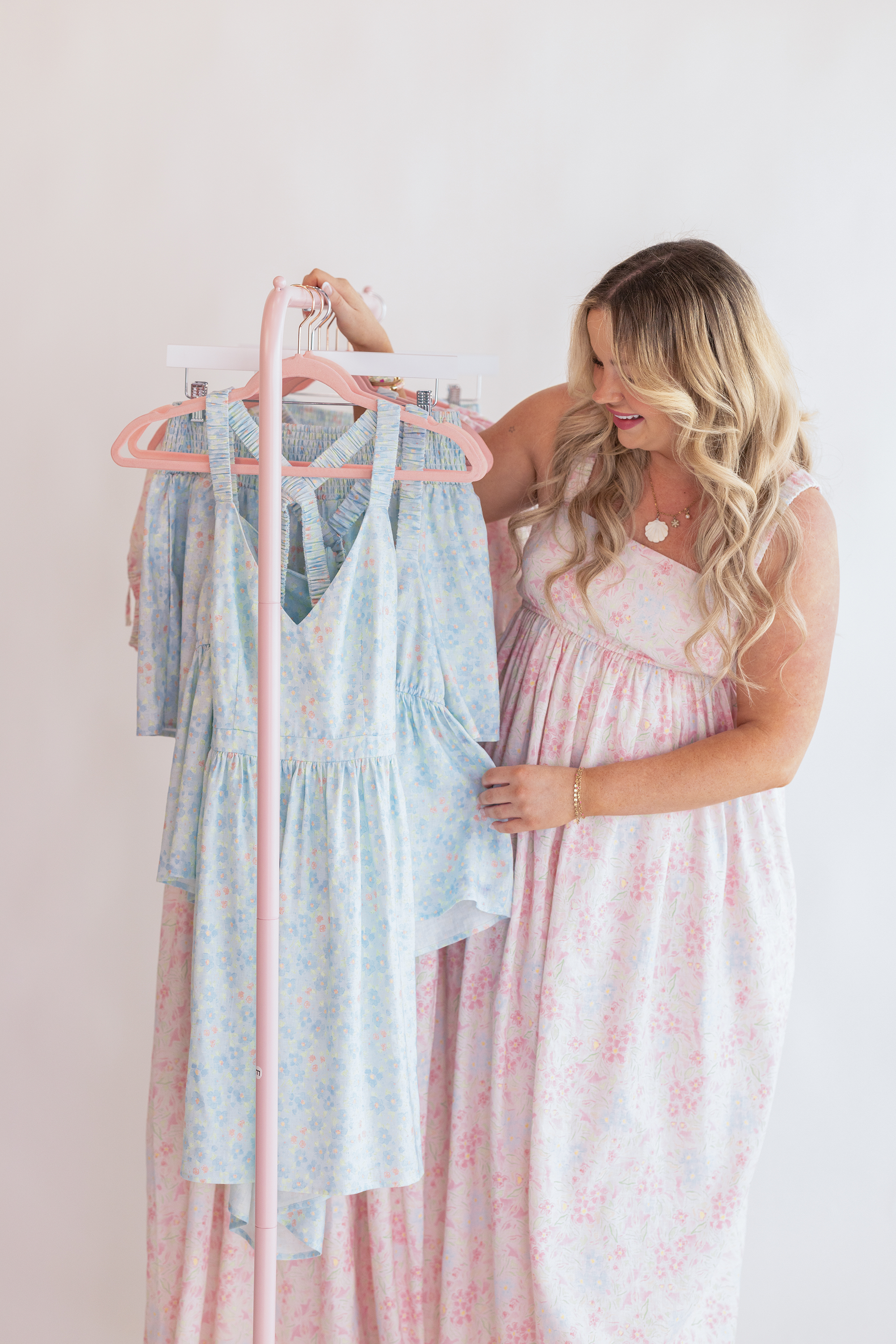 Woman wearing a long pink dress, touching other blue dresses on hangers